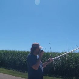 man holding a ham radio antenna near a cornfield