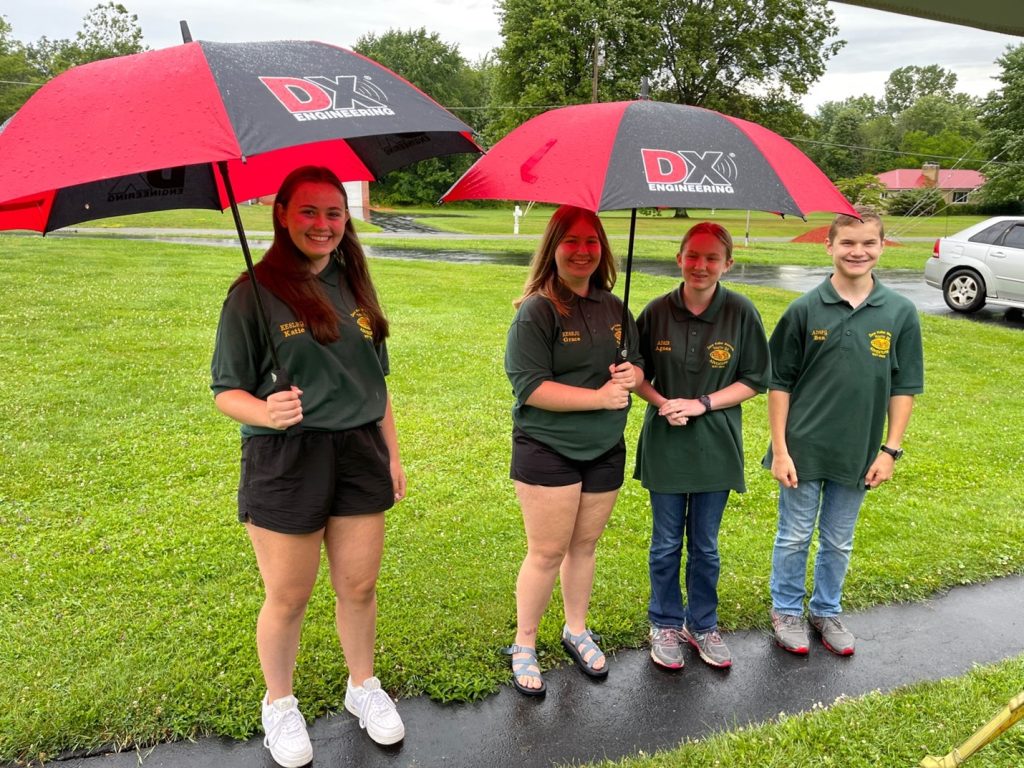 a group of young ham radio operators standing under umbrellas outside in the rain
