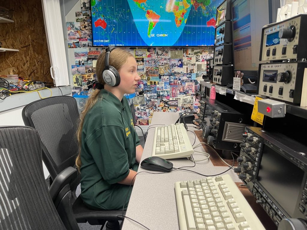 young lady sitting at controls of an amateur ham radio station