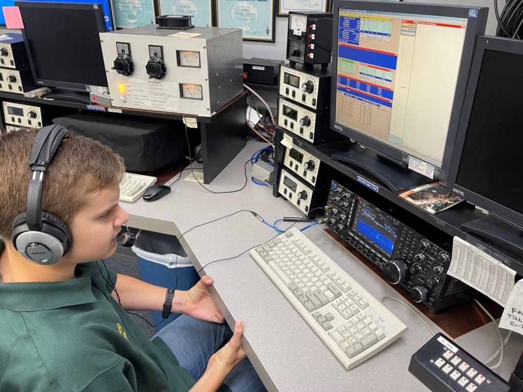 young man sitting at desk of a large amateur ham radio station