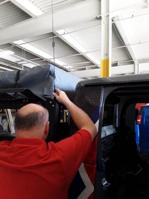 man installing a ham radio antenna on a jeep