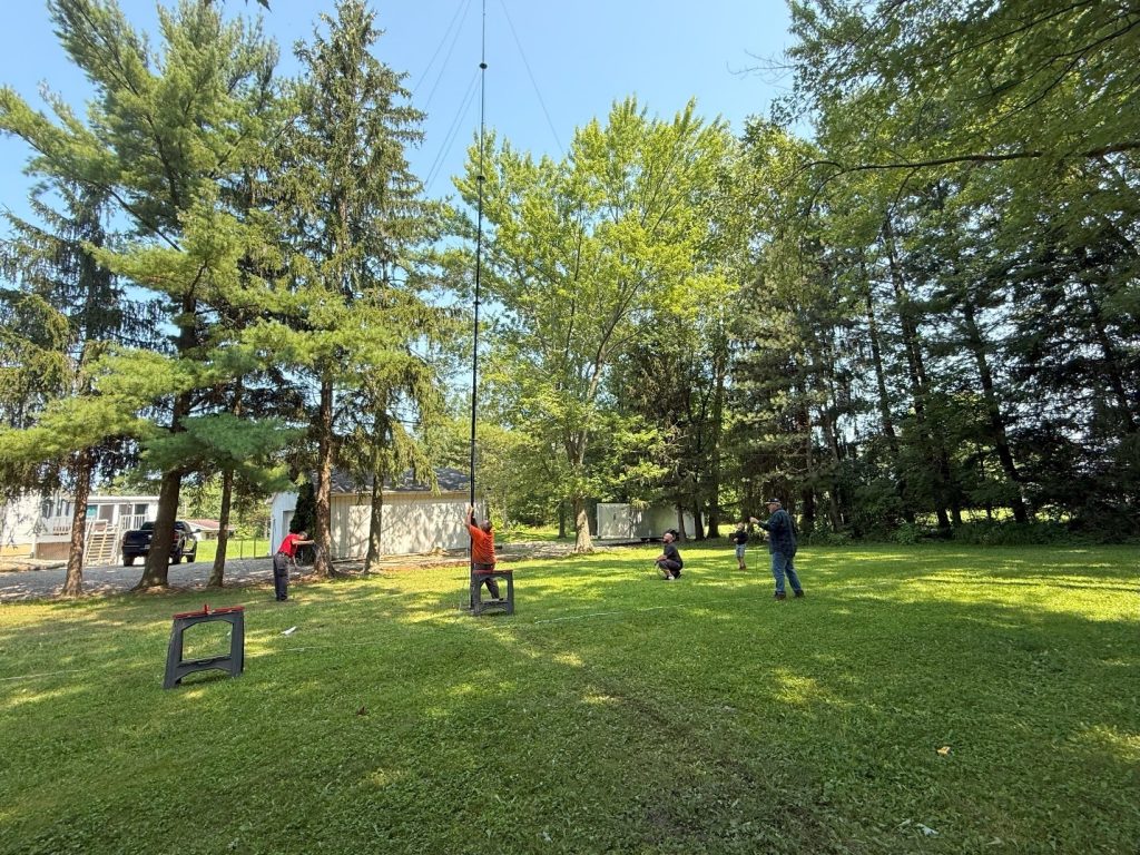 men putting a vertical antenna mast up in the air
